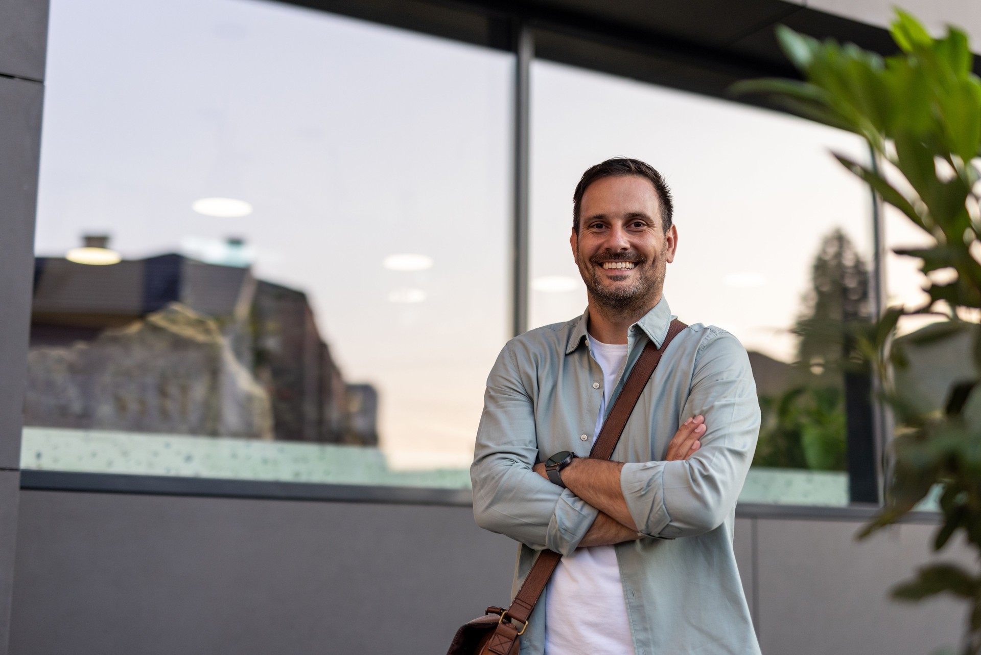 Portrait of smiling businessman standing with arms crossed in front of modern office building